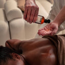 Masseur versant de l'huile de jojoba ZenGrowth dans sa main avant un massage du dos, client couvert d'une serviette Serenza marron